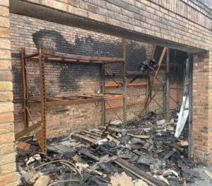 Burned warehouse interior showing damaged pallet rack beams and debris after fire
